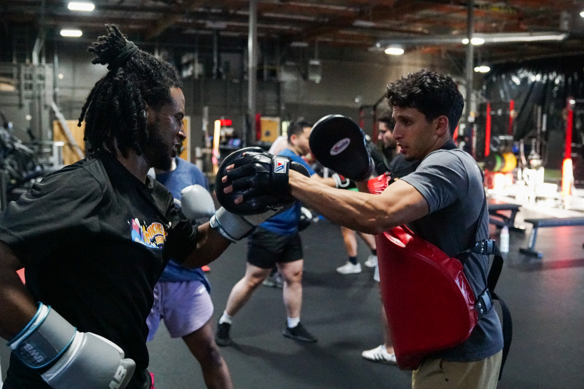 Group Classes — Coach Bakr holding mitts for a student mid-cross during an all-levels group class at BWB