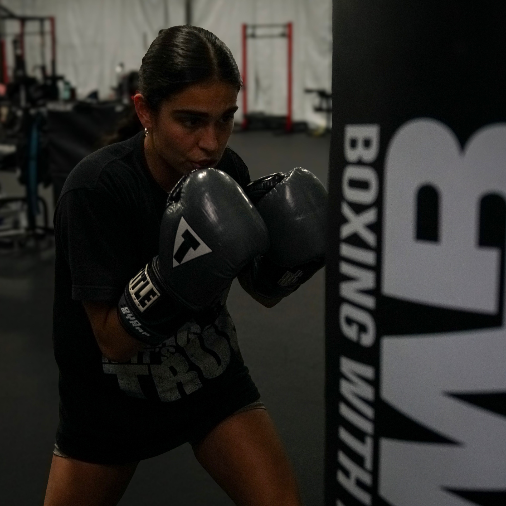 Coach Bella on the heavy bag at Boxing With Bakr, gloves up in stance