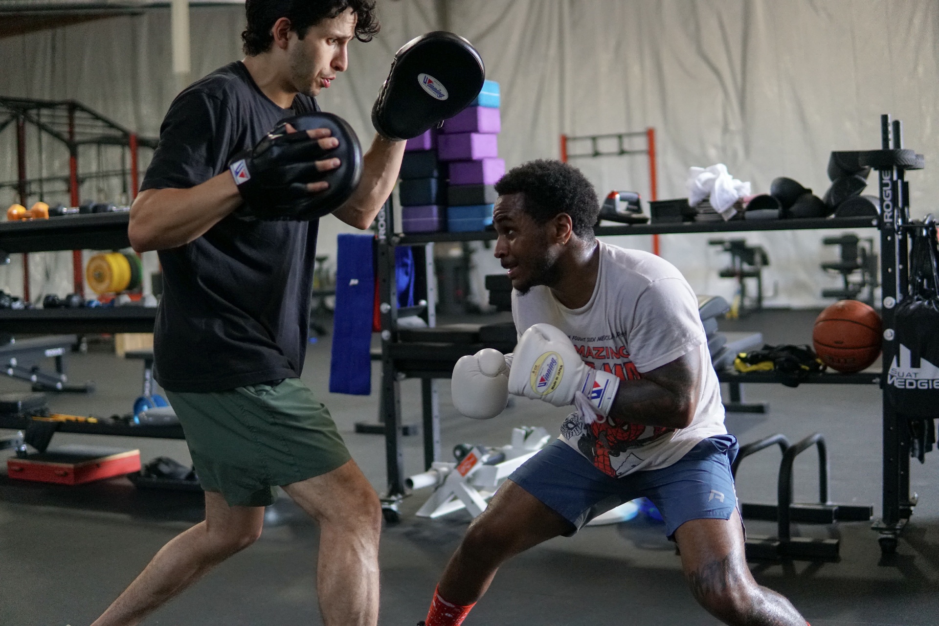 Steve in a deep crouch loading up on the mitts with his coach, eye contact
